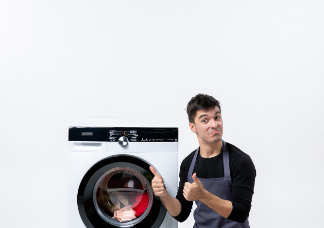 Man in apron giving thumbs up near washing machine. Same-day repair in Dubai.