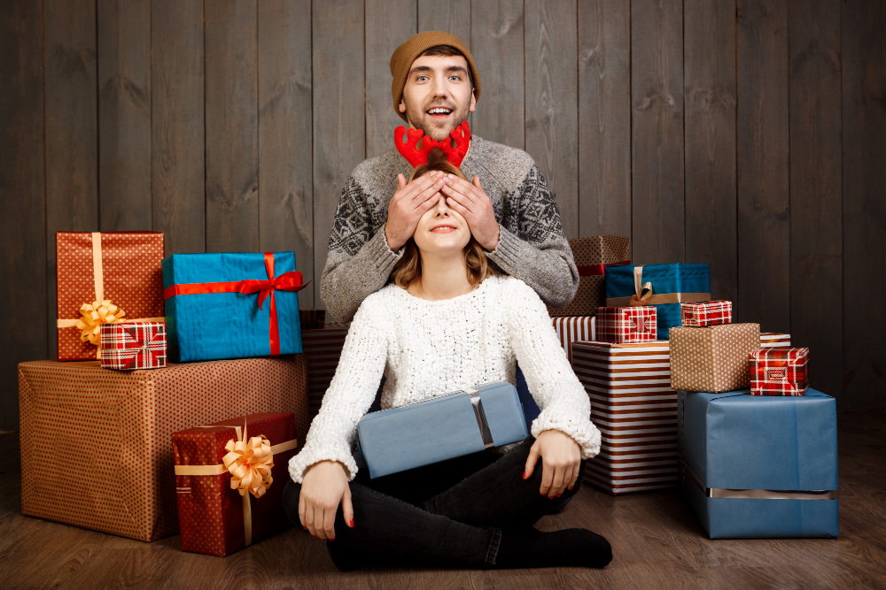 A man and woman sit on a wooden floor surrounded by colorful presents, celebrating meaningful gift ideas for special occasions.