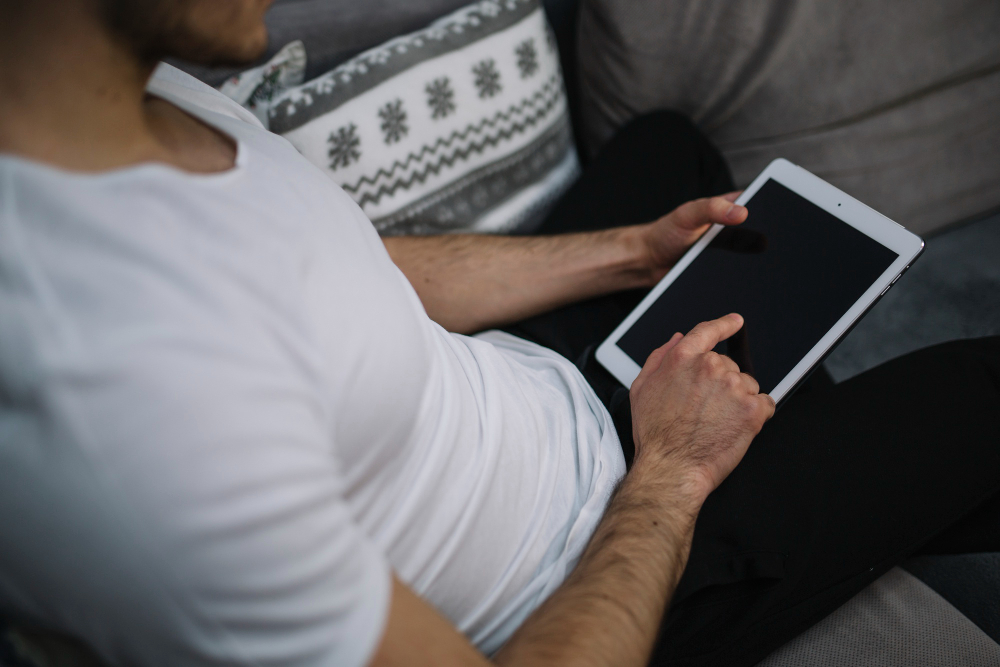 A man on a couch, engaged with a tablet, demonstrating the We2usat K3 Pro and vSeeBox V3 Plus in 2025.