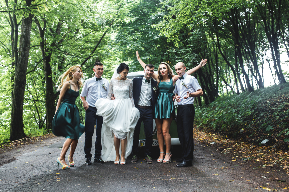A group of people smiling and posing beside a decorated wedding car, representing Group Travel Experts for weddings in NC.