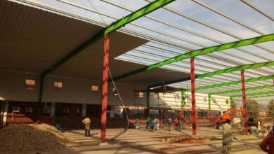 Construction of a pre-engineered steel building with green beams and red columns.