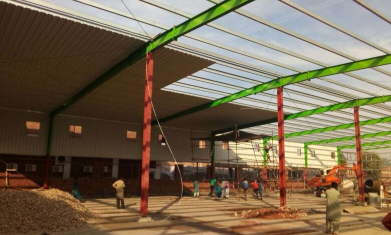 Construction of a pre-engineered steel building with green beams and red columns.