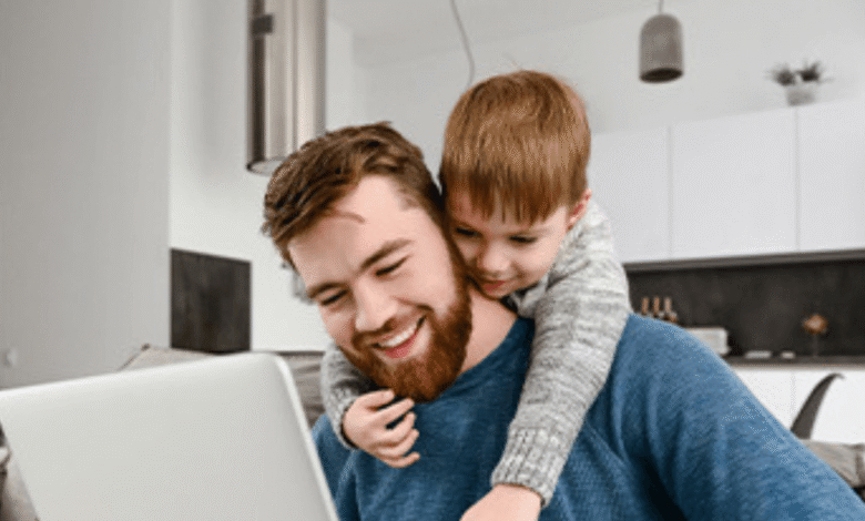 A man and a child are seated on a couch, engaging with a laptop placed on their laps