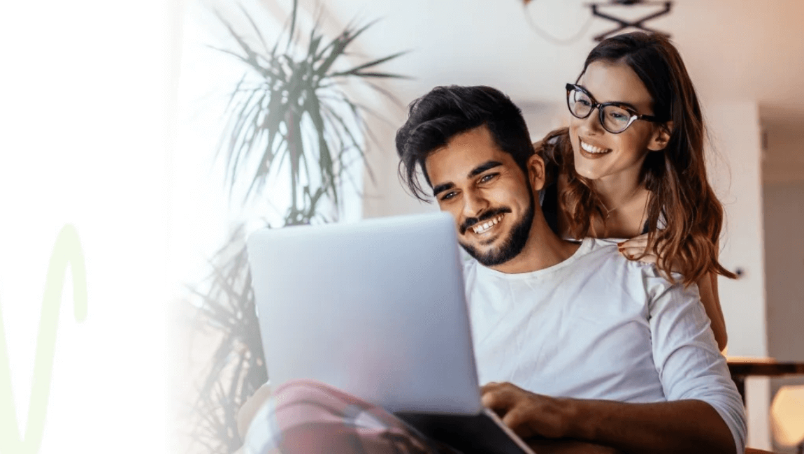A man and woman relax on a couch, sharing a moment as they view a laptop together